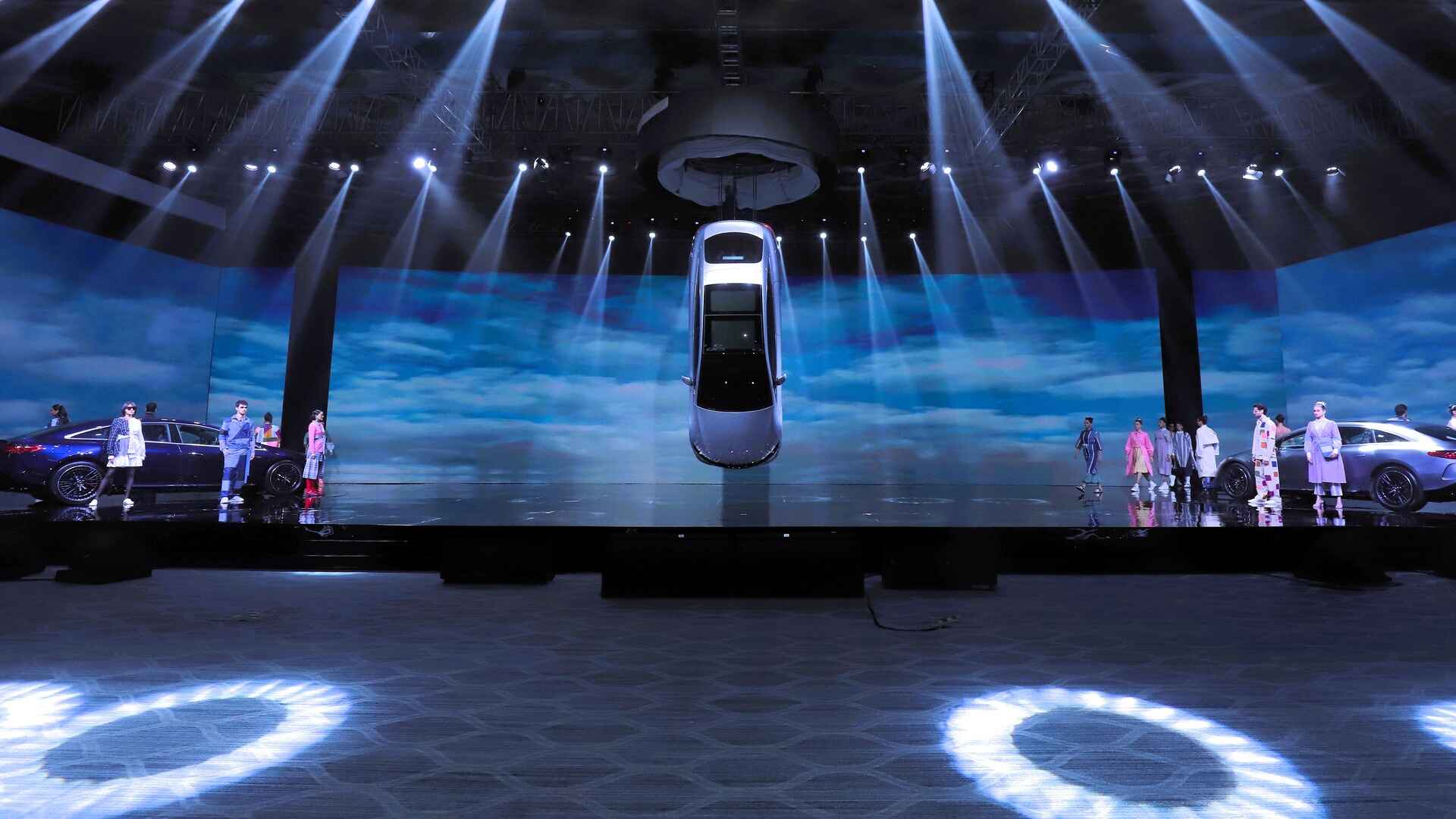 A Mercedes-Benz EQS suspending overhead, and models wearing designs by Kriti Tula standing alongside two Mercedes-Benz EQS.