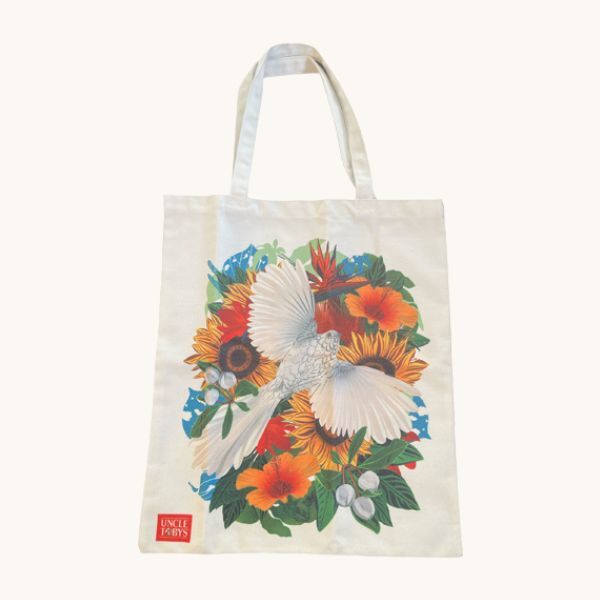 A beige tote bag adorned with a white bird and floral designs, showcasing a cheerful nature theme.