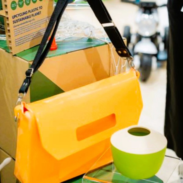 PMG-Thailand-Innovation-Day-2024-3.jpg A yellow ladies' bag refashioned from rubber gloves rests on a table beside a green and white vessel, creating a vibrant and stylish arrangement.