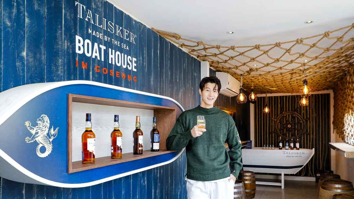 Actor Li Ki-Woo stands in front of a bar counter that says Talisker Made by the Sea: Boathouse in Goseong, featuring Talisker whiskies.